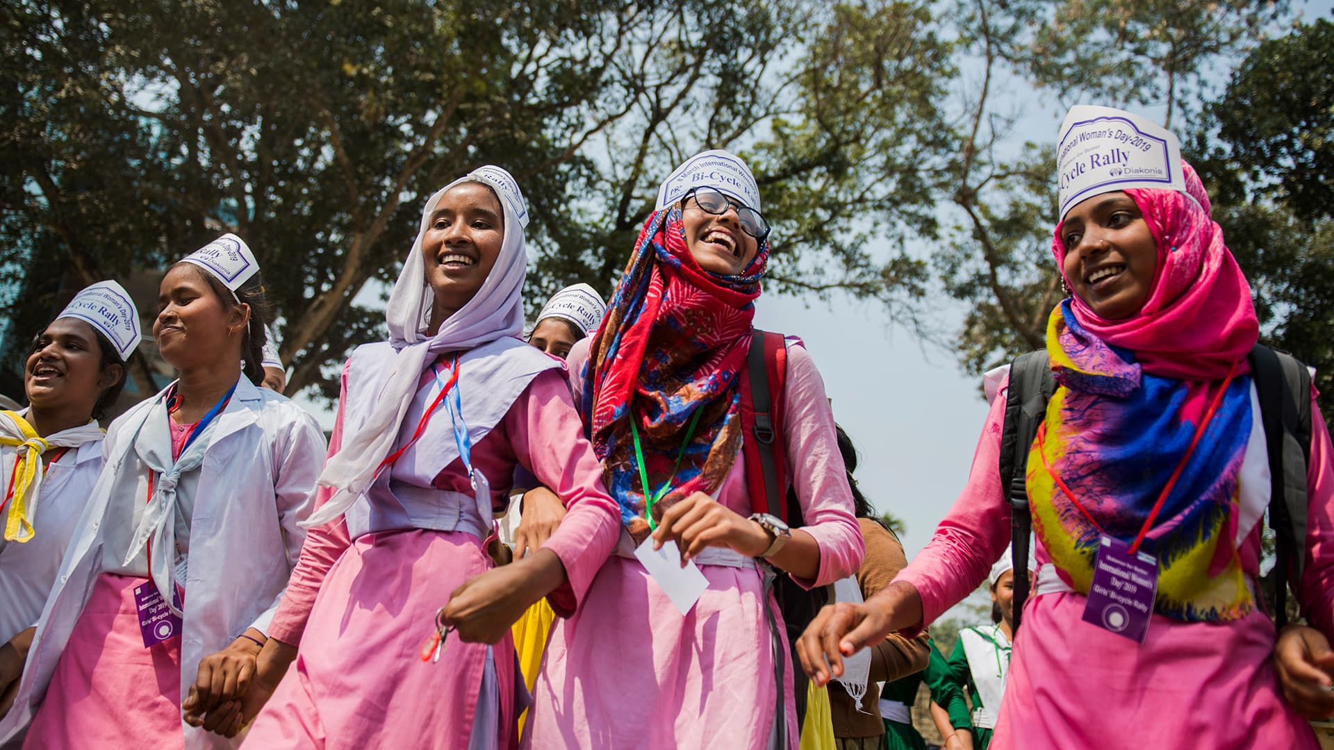 A group of young women at a manifestation. They are jolding hands and smiling.