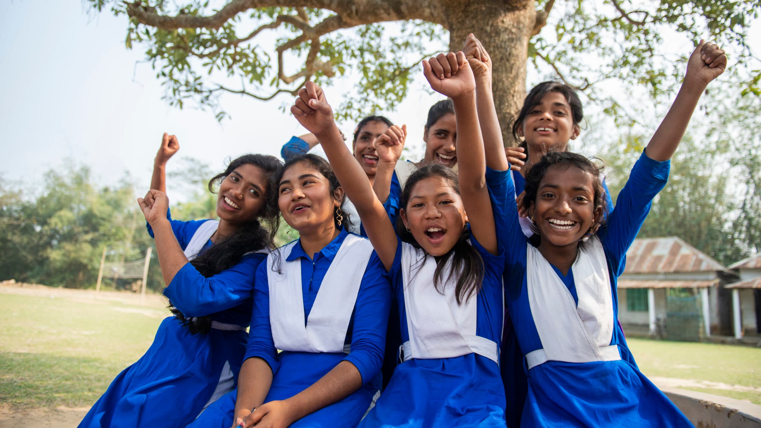 Photo: Gustav Hugosson A group of girls in school uniforms sitting next to a tree. They are lifting their hands up.