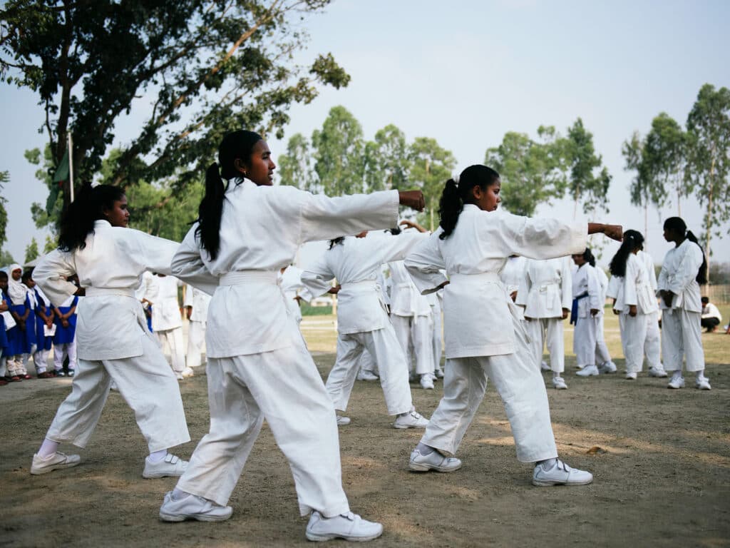 Photo: Gustav Hugosson A large group of young women in white karate suits, standing in karate positions.