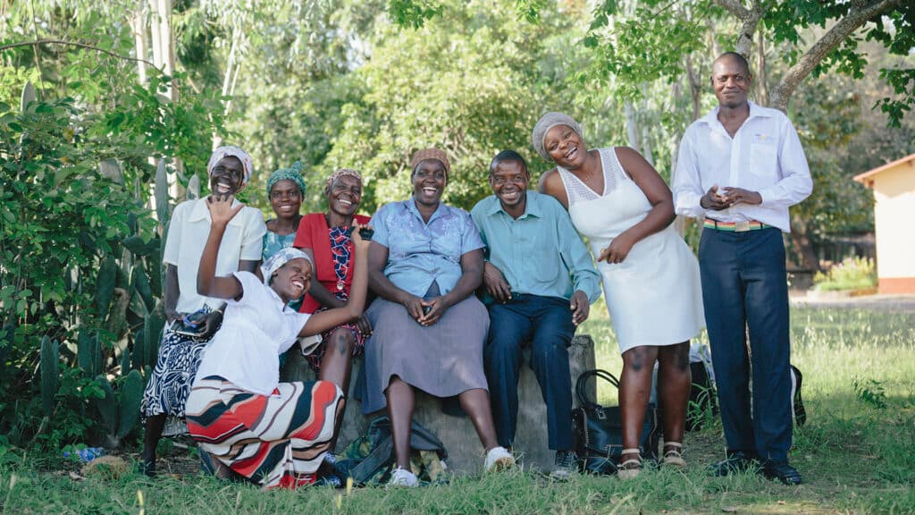 A group of Zimbabwean men and women outside in a green field with trees in the background.