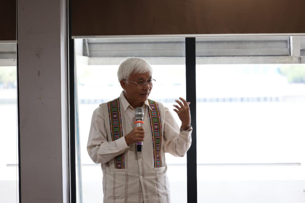 Sakda speaks passionately, dressed in a traditional vibrant vest, during a public meeting.