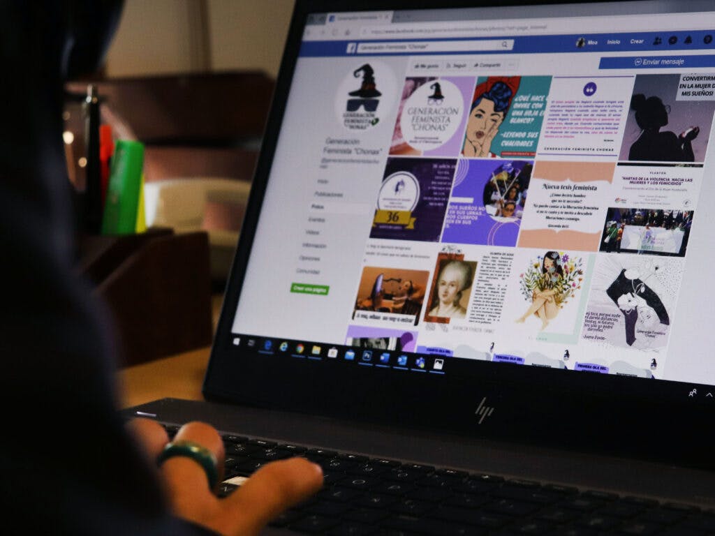 En person med ryggen mot kameran har handen på ett tangentbord på en laptop. På skärmen syns en Facebook-sida med olika bilder.