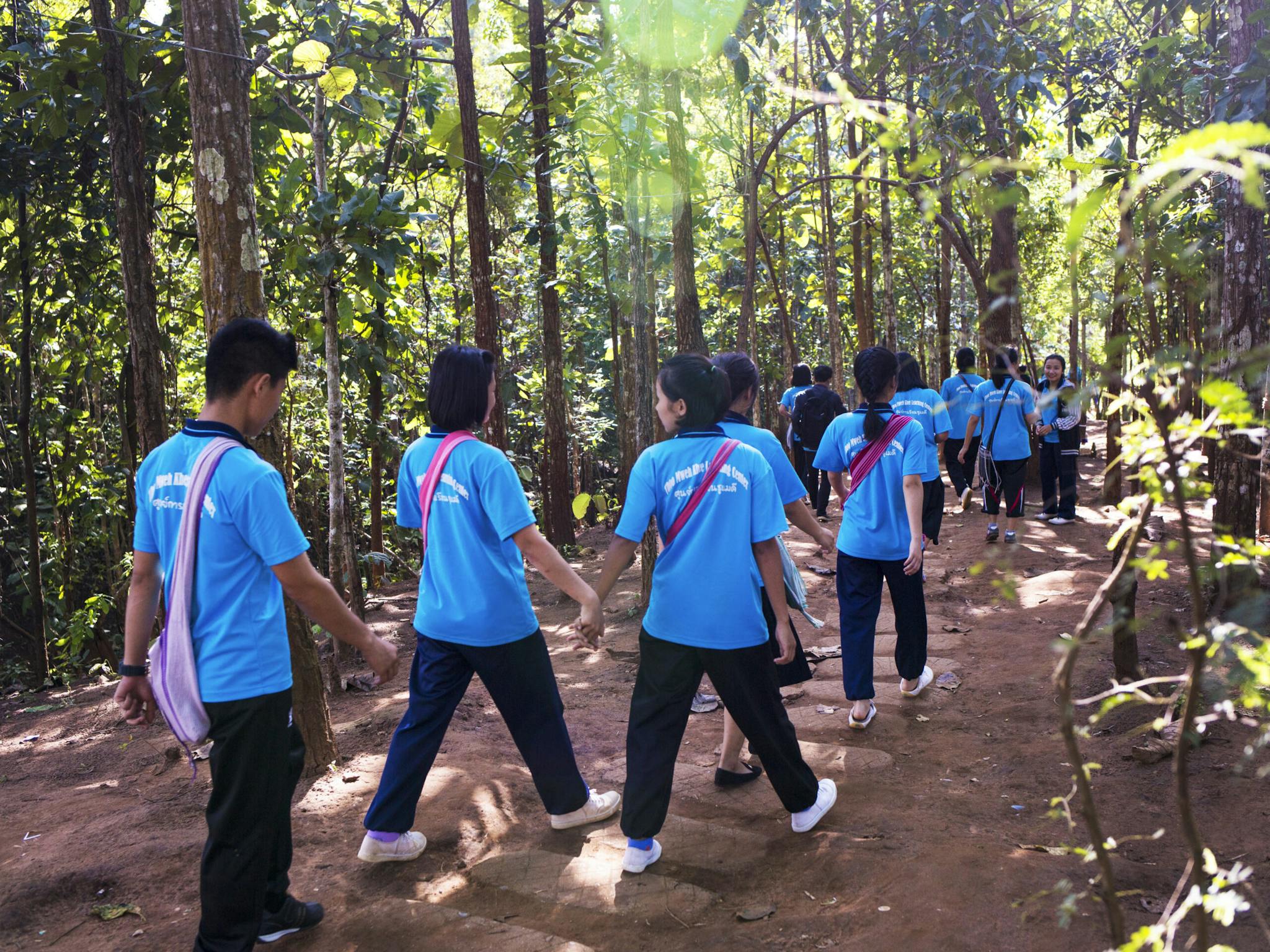 Flera människor i likadana ljusblåa t-shirts med text på ryggen går genom ett skogsområde, några håller varandra i handen.