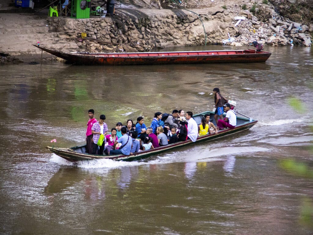 Bild av en lång motorbåt som åker i en flod. I båten sitter flera vuxna och barn.