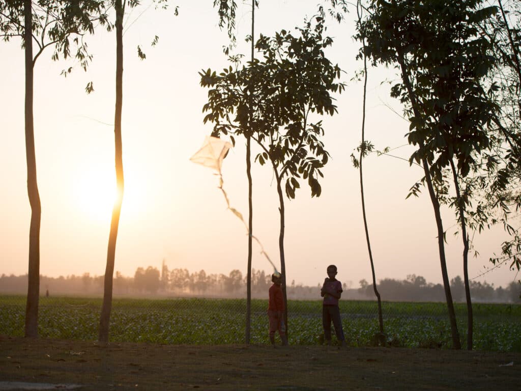 Två barn leker med en drake i solnedgången
