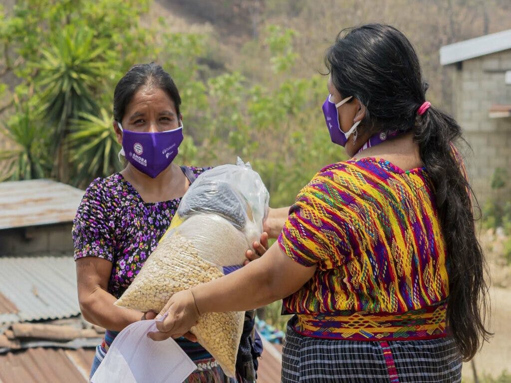 Två kvinnor i Guatemala med munskydd bär på matpaket