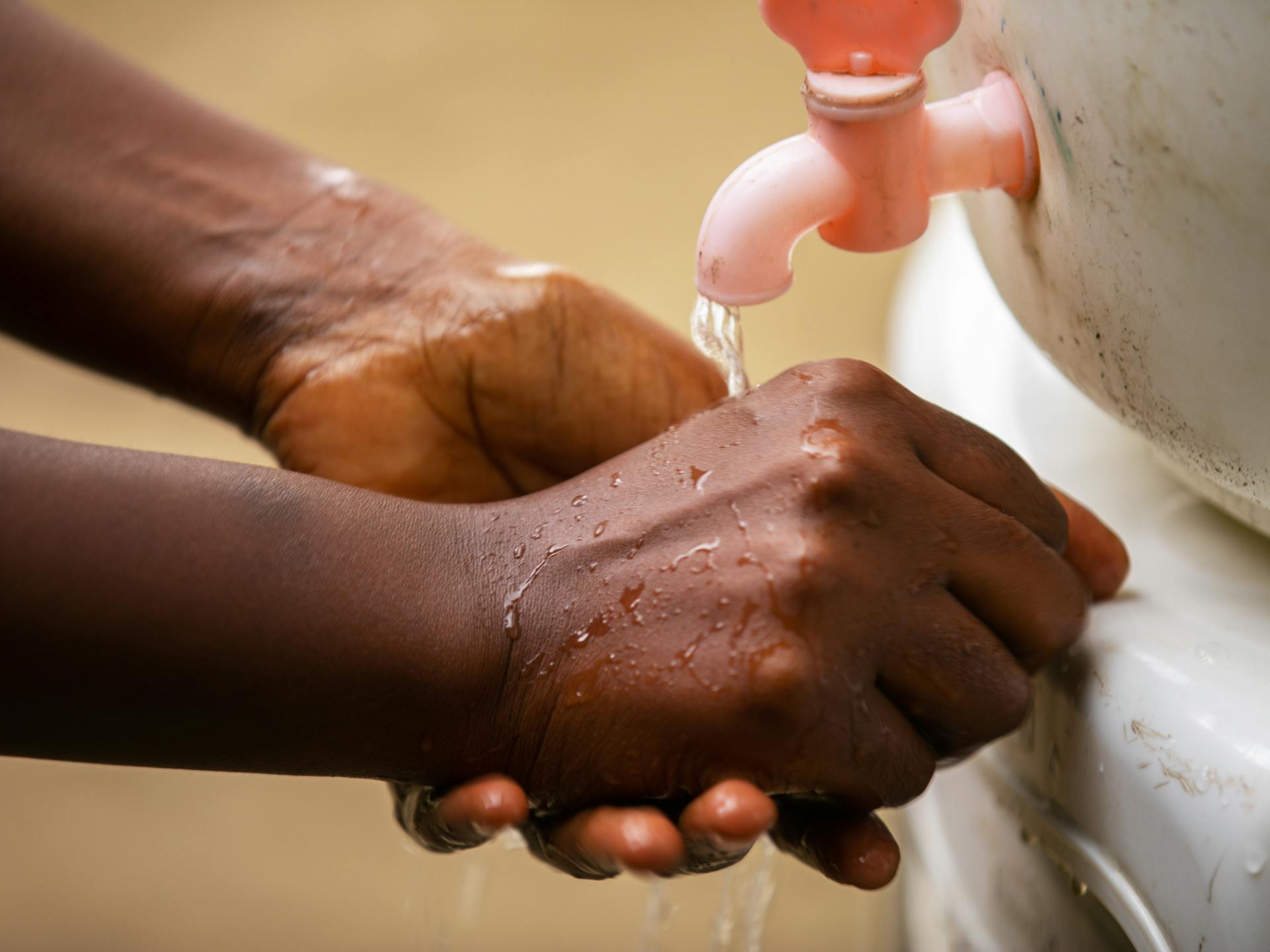 Närbild på två händer som tvättar sig med vatten från en plastkran.