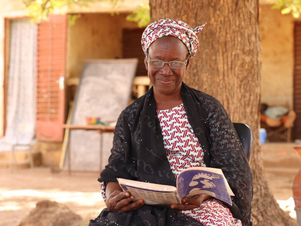 En äldre kvinna tittat in i kameran med en bok i knät