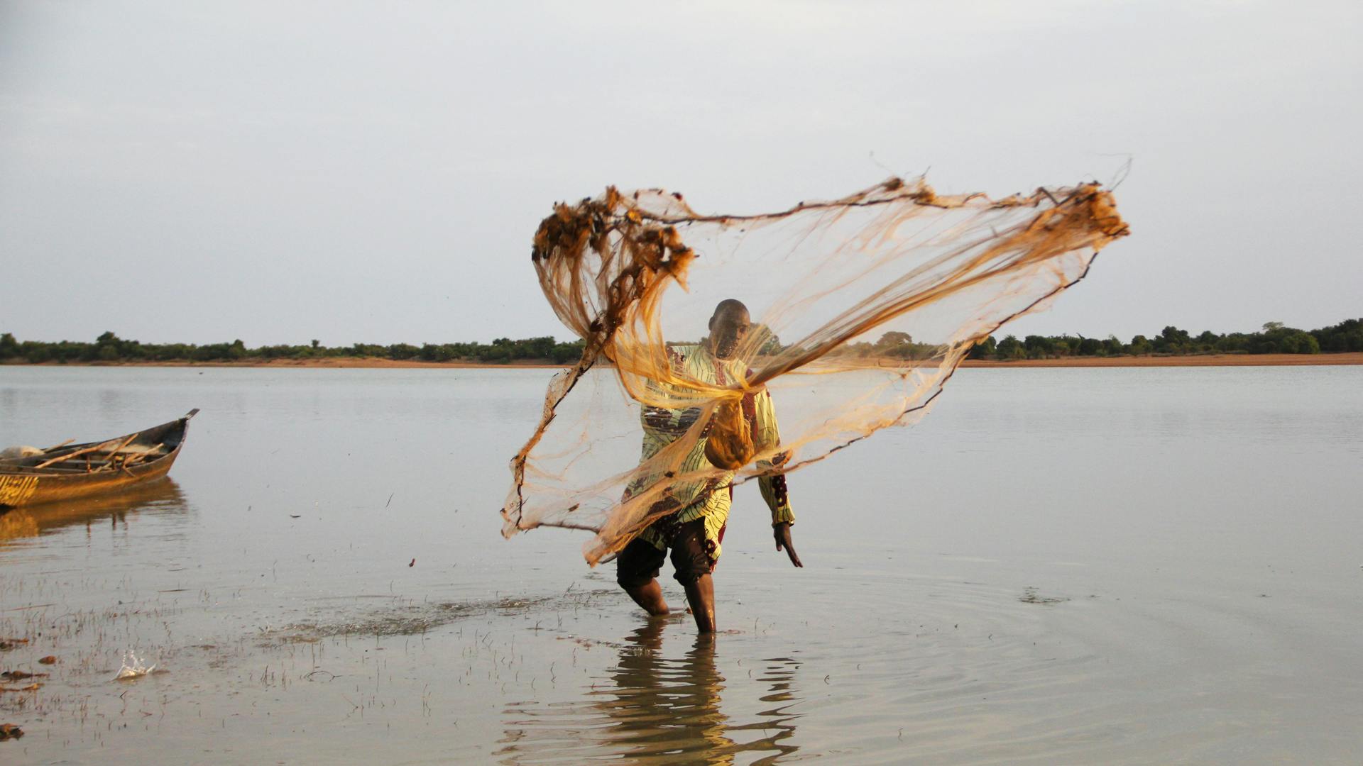 En fiskare står i vattnet och kastar ett nät