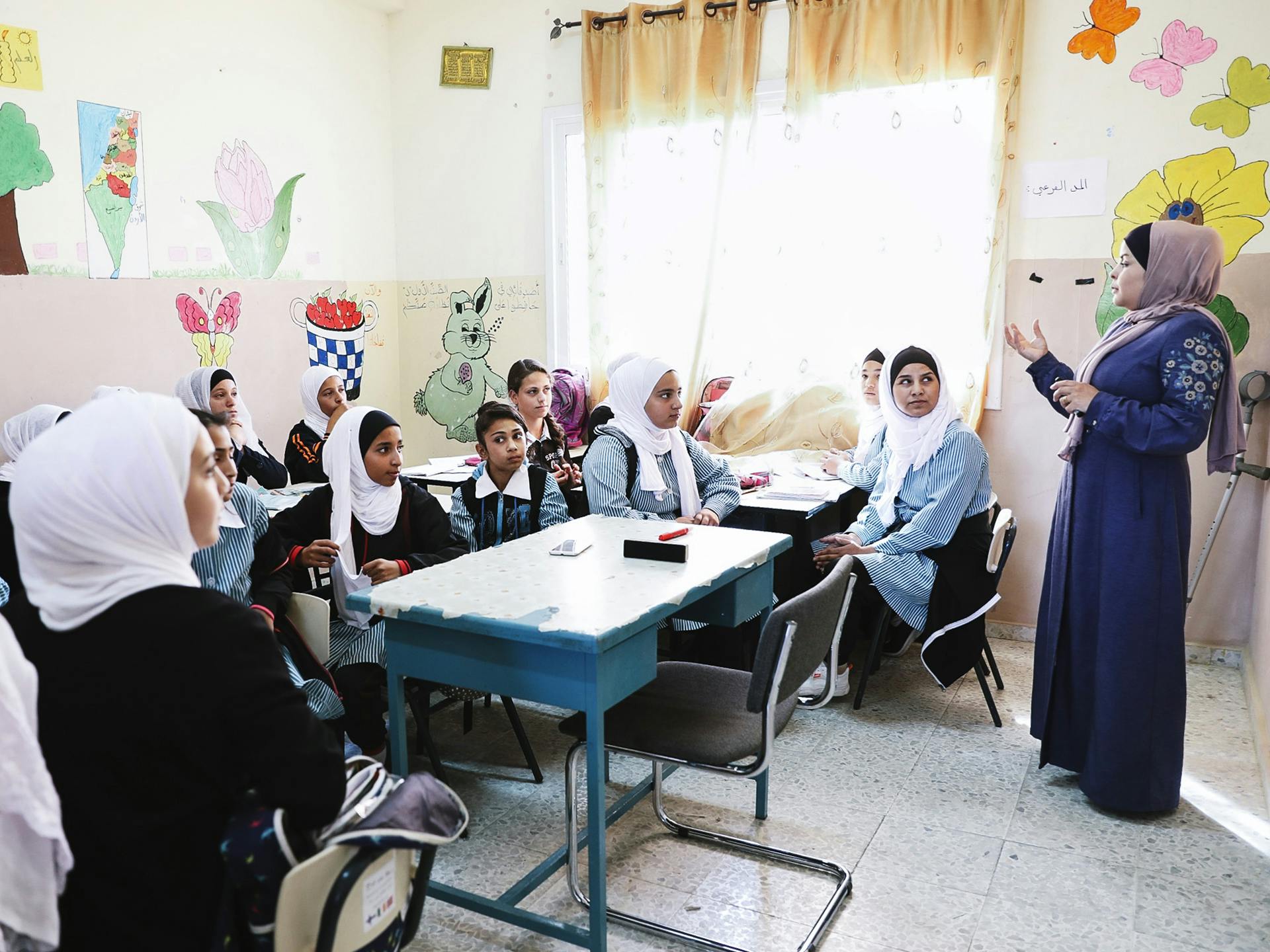 Ett klassrum i Palestina med unga flickor och en lärare. Väggarna är målade med olika motiv.