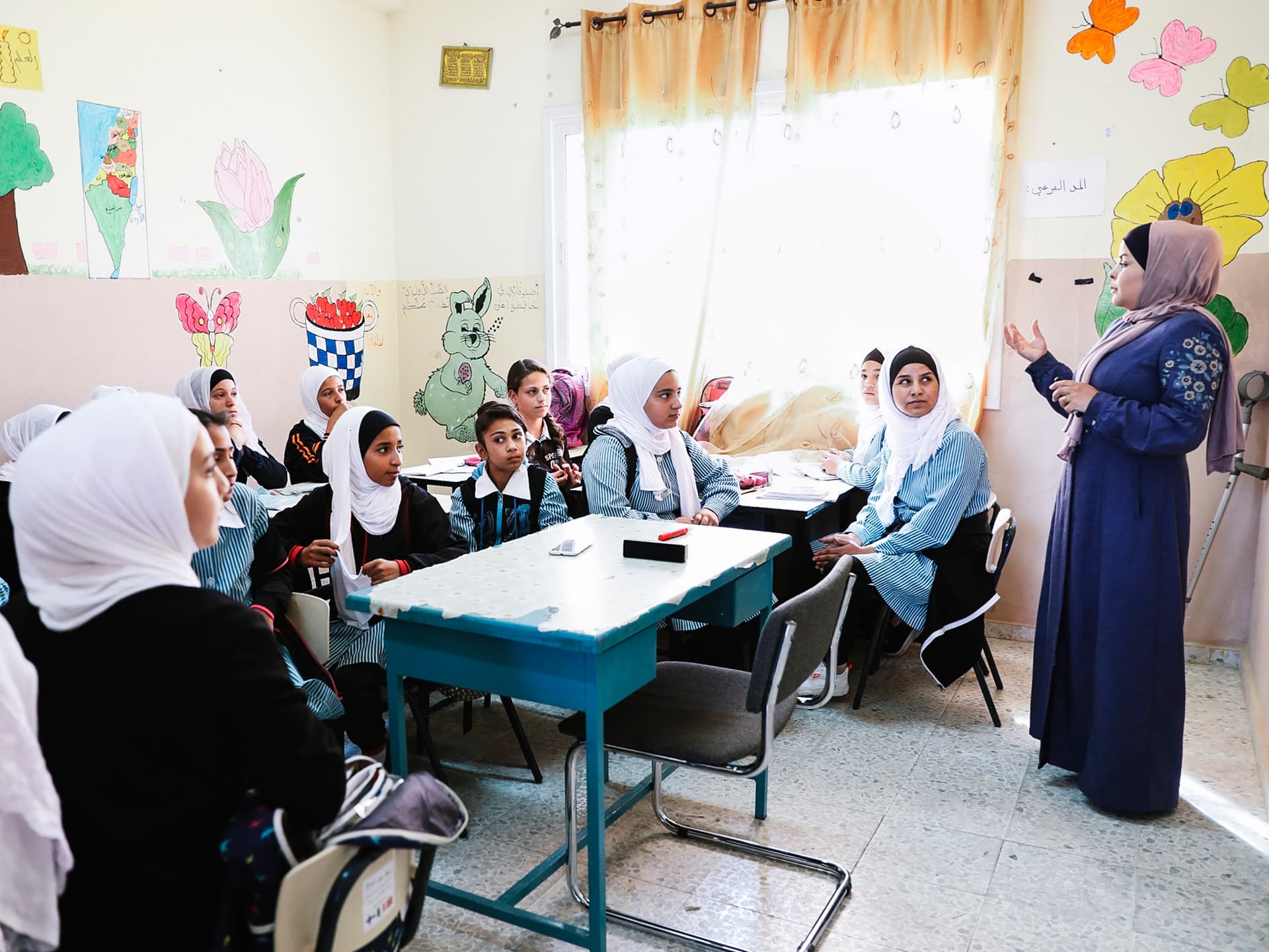 Foto: Diakonia Ett klassrum i Palestina med unga flickor och en lärare. Väggarna är målade med olika motiv.