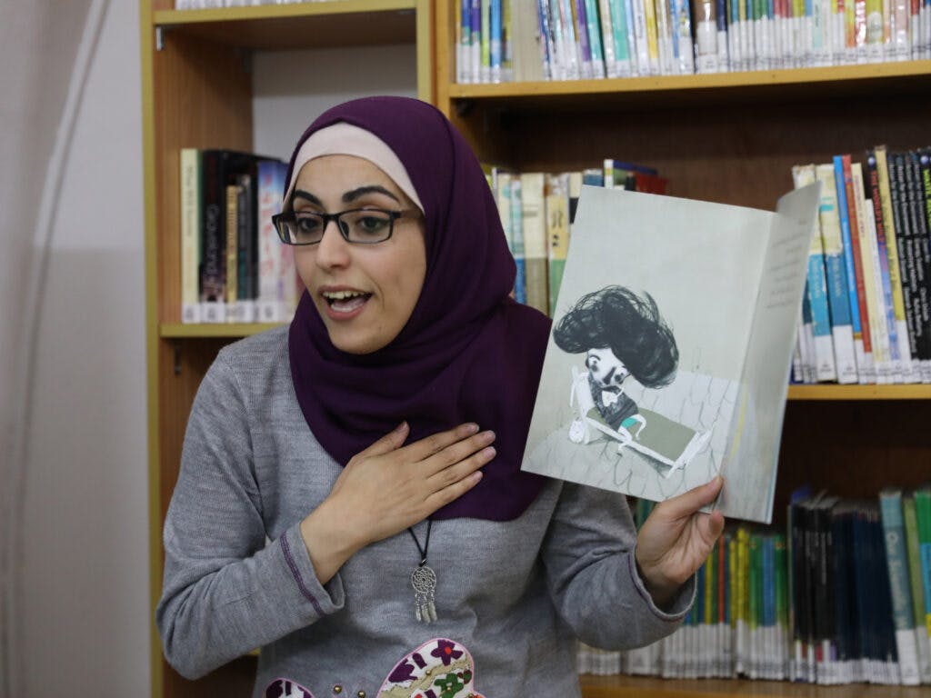 En kvinna i ett bibliotek visar en bilderbok och läser