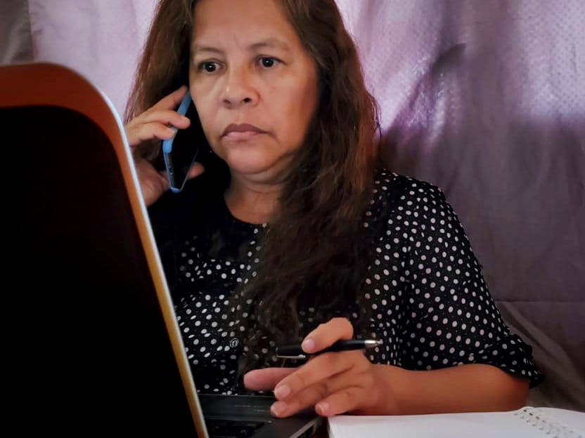 En kvinna sitter med en telefon mot örat framför en dataskärm.