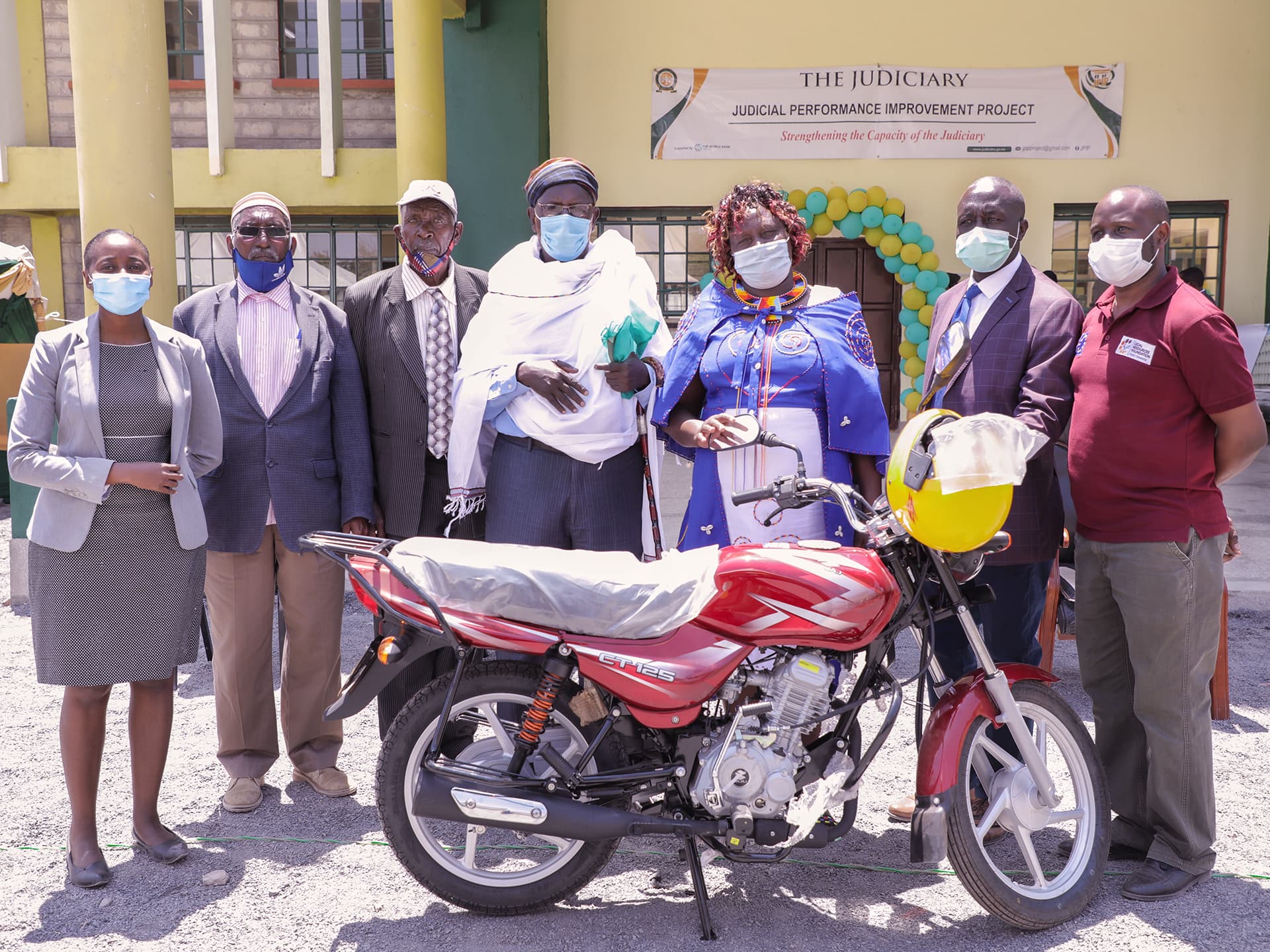 Foto: Legal Resource Foundation En grupp människor står framför en byggnad med en motorcykel framför sig.