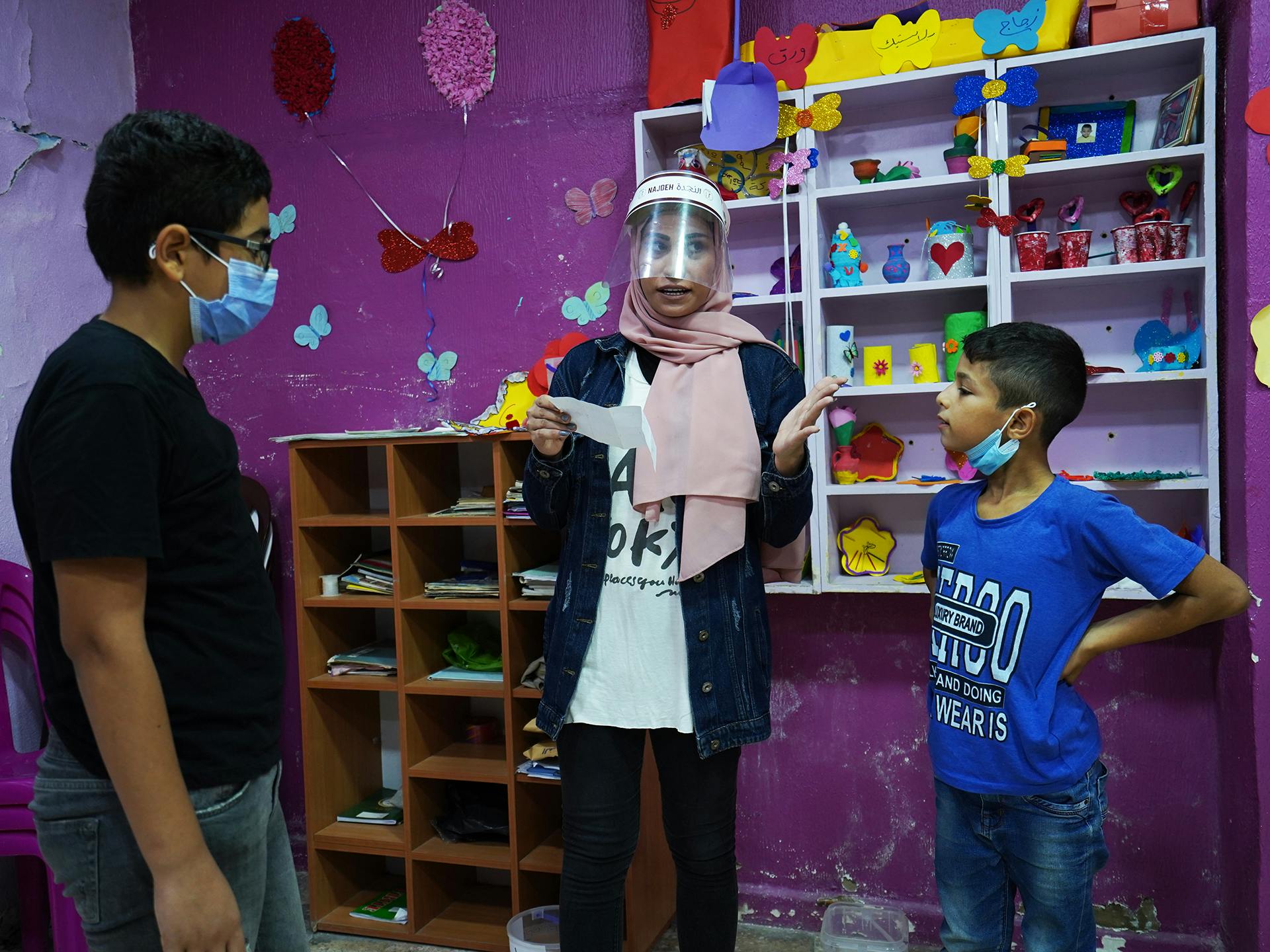 En lärare och två barn stor i ett rum med rosamålade väggar och bokhyllor med böcker.