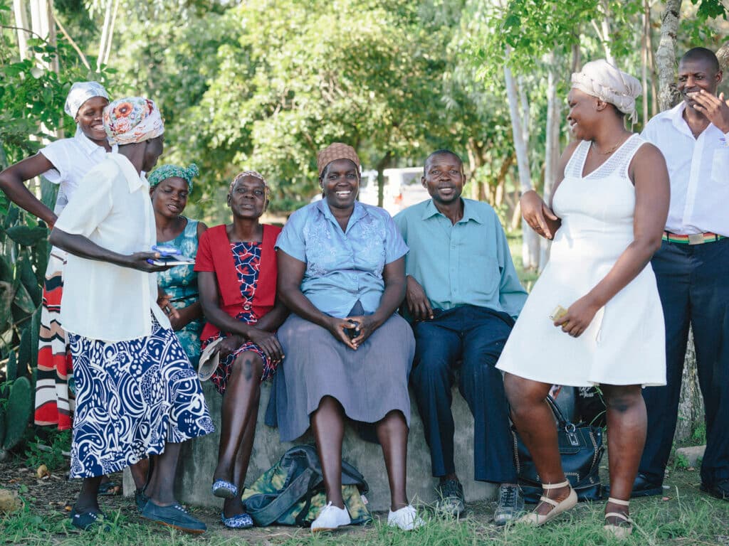 En grupp människor sitter framför gröna buskage och träd.