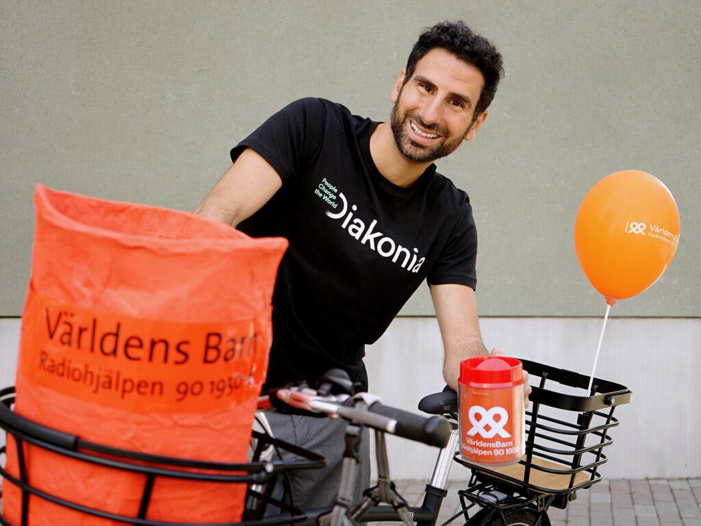 Stephan Wilson står med sin cykel i Diakonia-tröja och med en insamlingsbössa i handen.