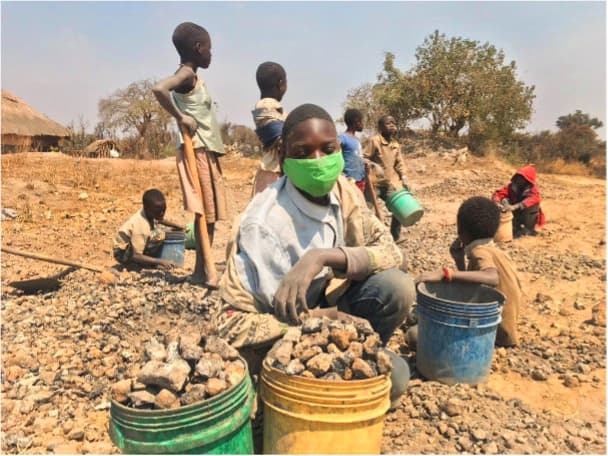 Foto: Diakonia En pojke med munskydd sitter på marken, framför sig har han några hinkar med sten.