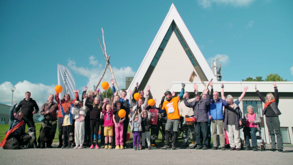 En grupp människor står framför en kyrka och sträcker händerna mot himlen och viftar med Världens Barn-ballonger