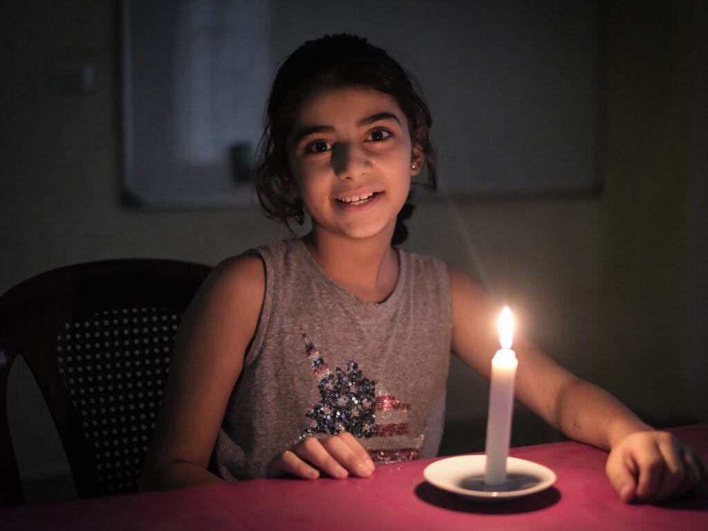 En leende flicka i ett mörkt rum med ett tänt ljus framför sig.