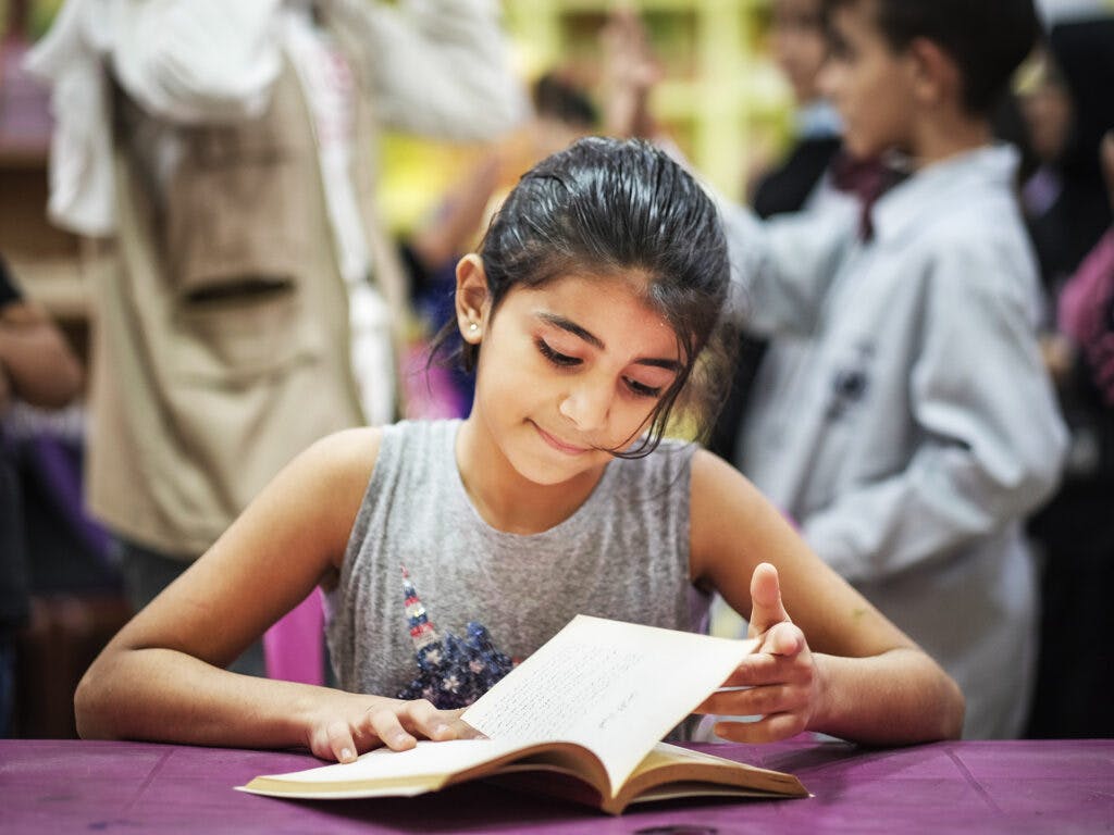 En flicka läser en bok i ett klassrum.