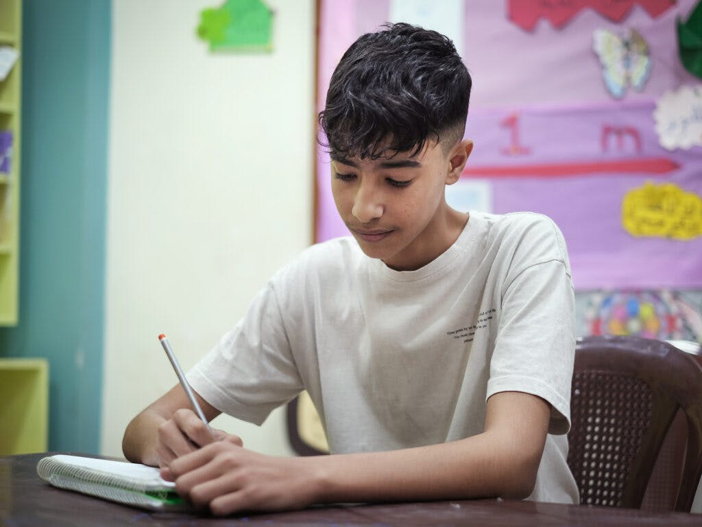 En ung pojke från Syrien vid en skolbänk skriver i en bok.