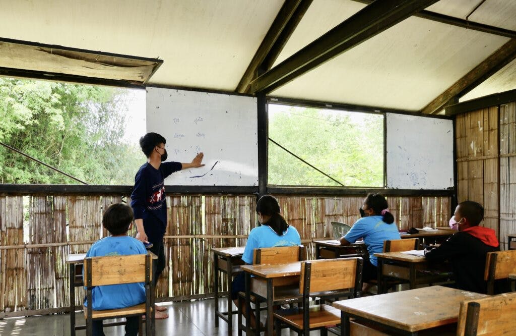 En lärare står framme vid tavlan i ett enkelt klassrum