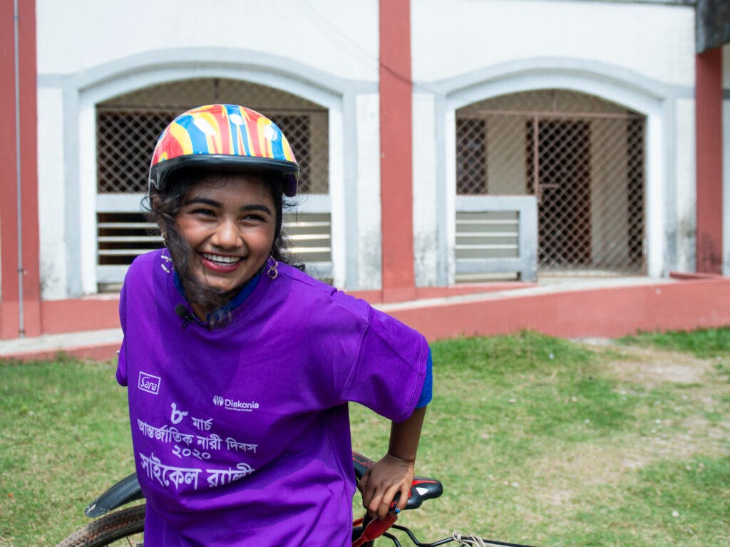 En flicka i lila t-shirt och cykelhjälm som ler.