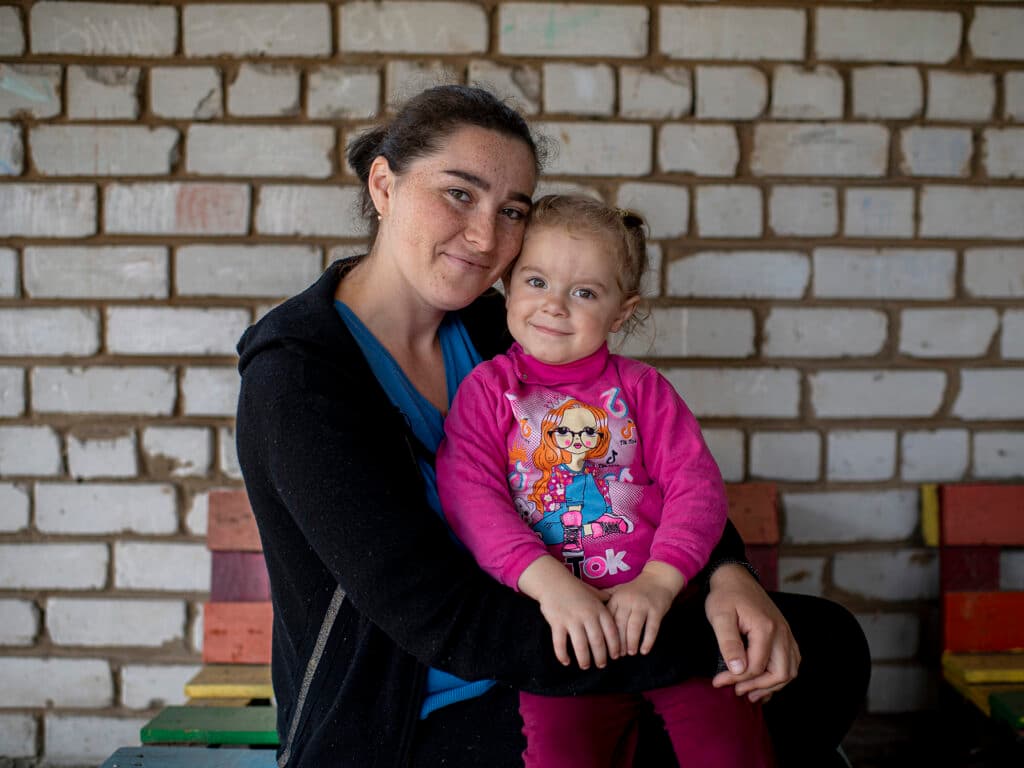 Foto: Andras D. Hajdu/Act Alliance En kvinna med ett barn i famnen ser in i kameran och ler.