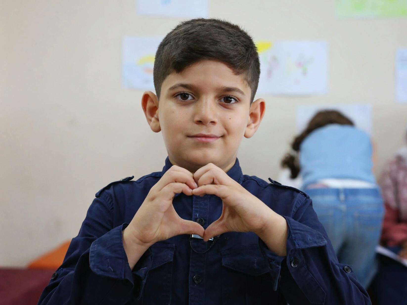 En pojke håller upp händerna som formas till ett hjärta.