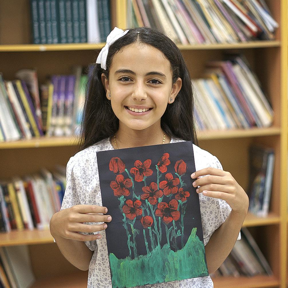 En flicka håller upp en teckning. På teckningen är det röda blommor mot svart bakgrund.