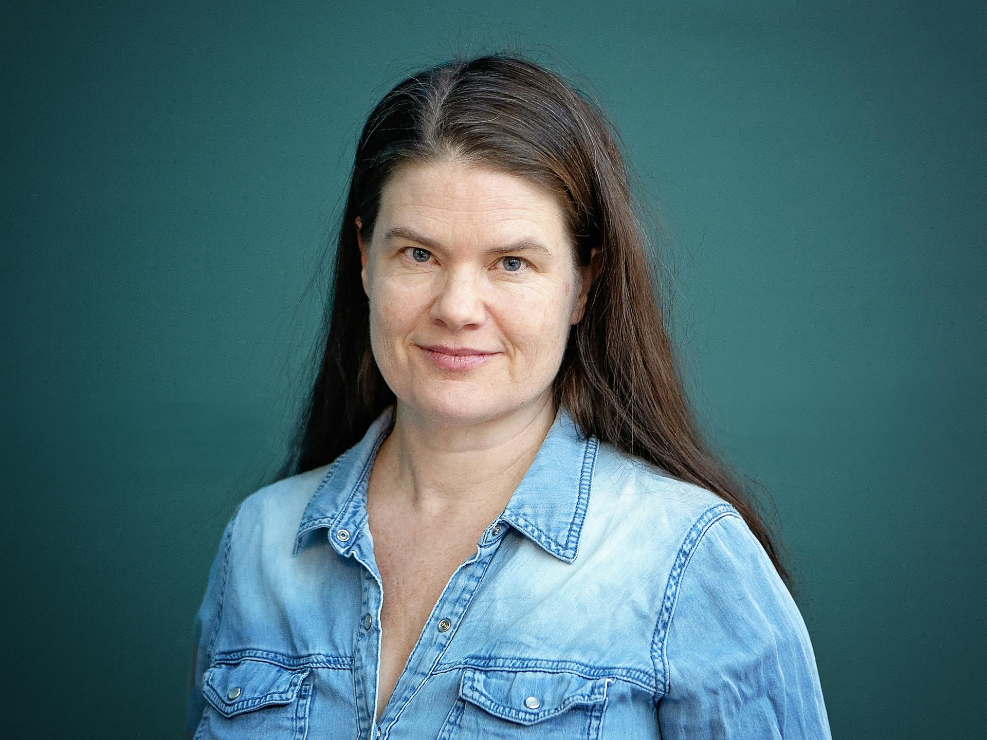 Ett porträtt av Jenny Enarsson mot blågrön bakgrund.
