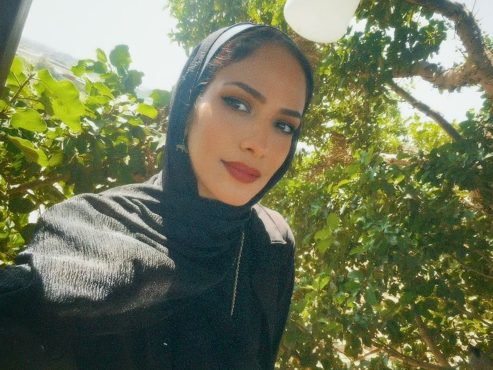 En kvinna i svart hijab med ett stort grönt träd i bakgrunden.