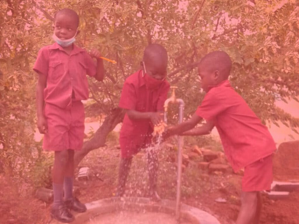 En bild av tre barn i skoluniformer som tvättar händerna vid en liten kran.