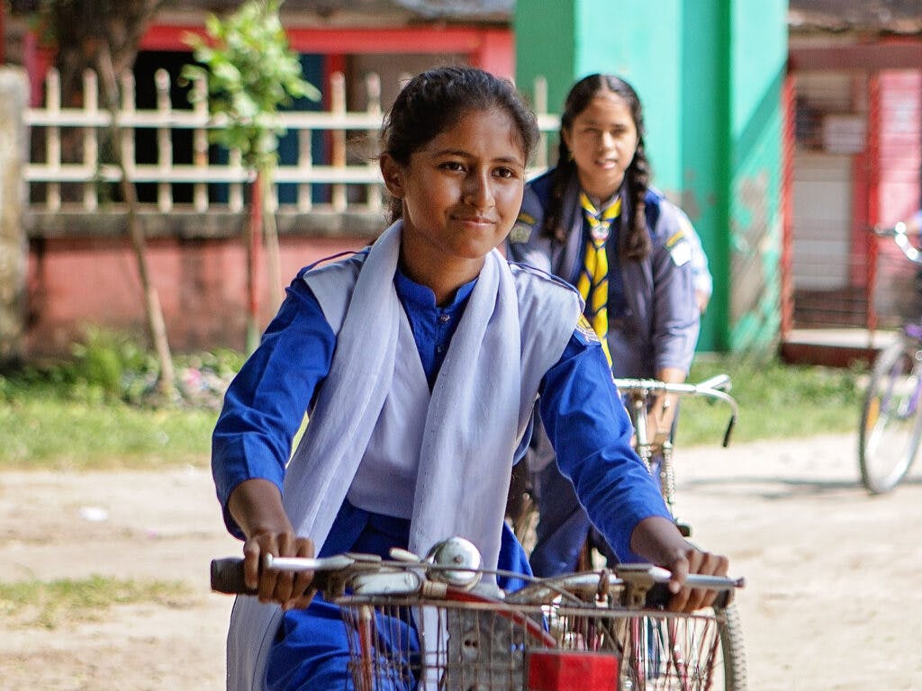 En flicka i skoluniform cyklar på en skolgård.