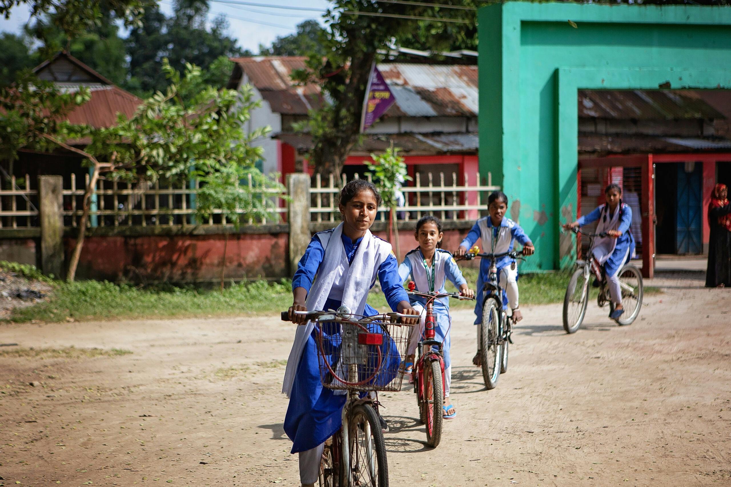 Fyra flickor i skoluniform cyklar efter varandra på en skolgård.