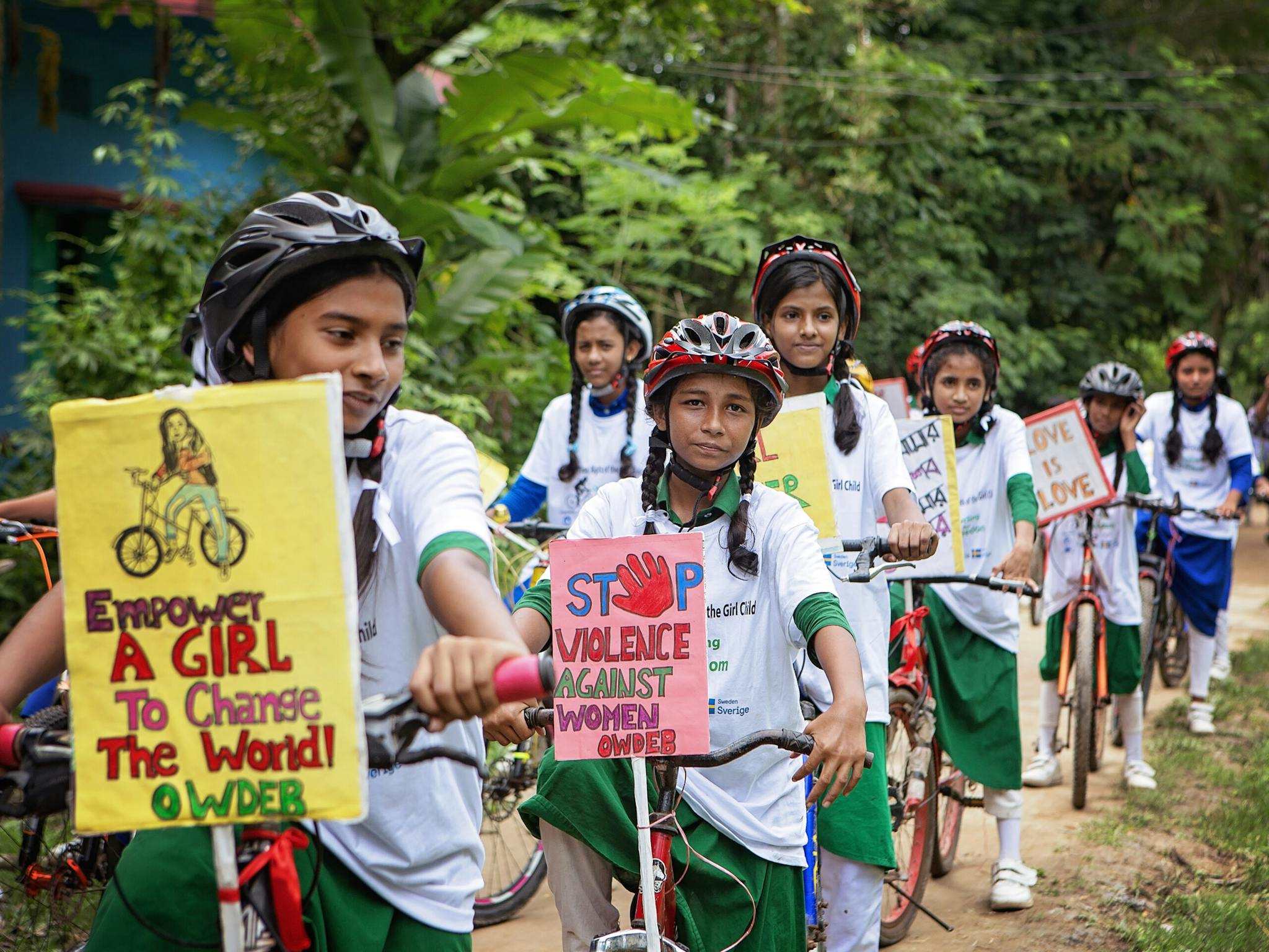 En rad av flickor i skoluniformer. Flickorna står med cyklar som har affischer med budskap för flickors rättigheter.
