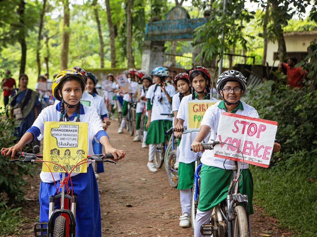 Flera tjejer i skoluniformer och cykelhjälmar står på rad med en varsin cykel.