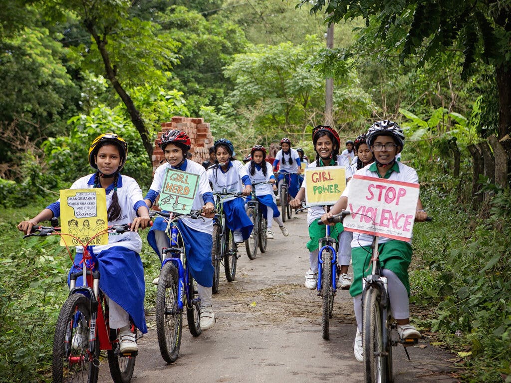 En rad av flickor i skoluniformer, cykelhjälmar och med varsin cykel står på led.