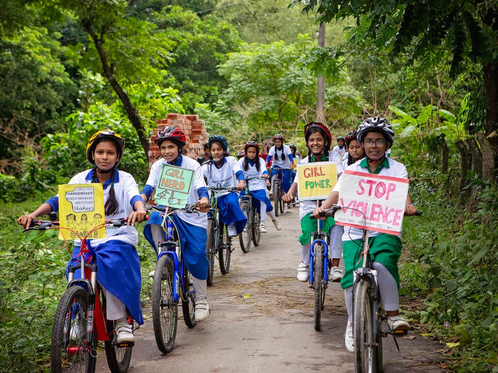 Foto: Diakonia En rad av flickor i skoluniformer, cykelhjälmar och med varsin cykel står på led.