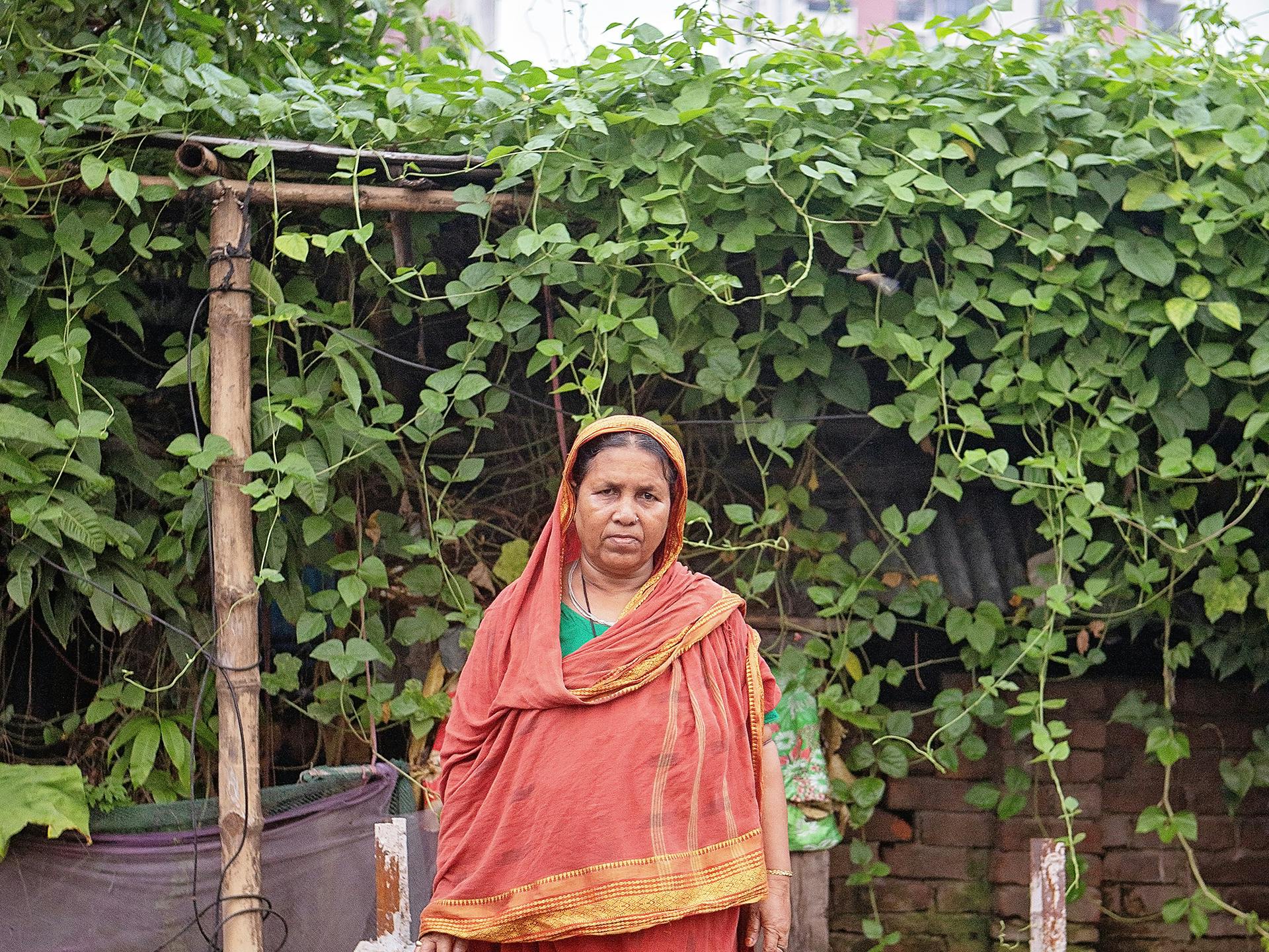 En kvinna i orange sari står mot en stor grön buske.