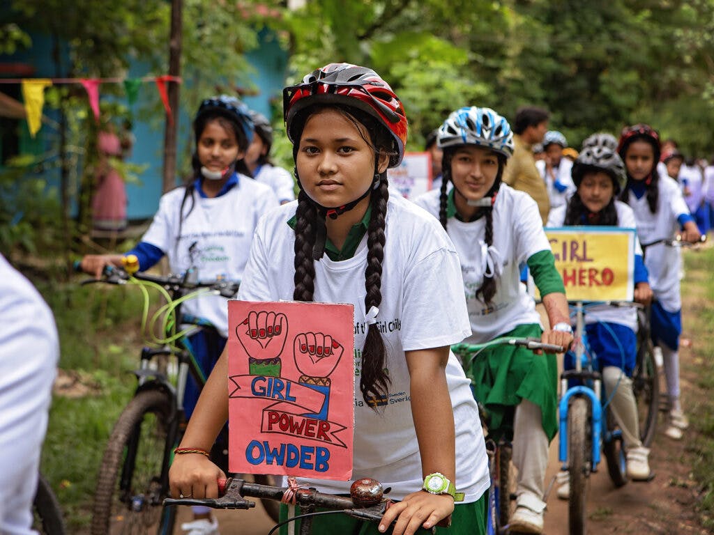 En flicka i cykelhjälm står med sin cykel, framför henne finns ett plakat med texten "Girl power".