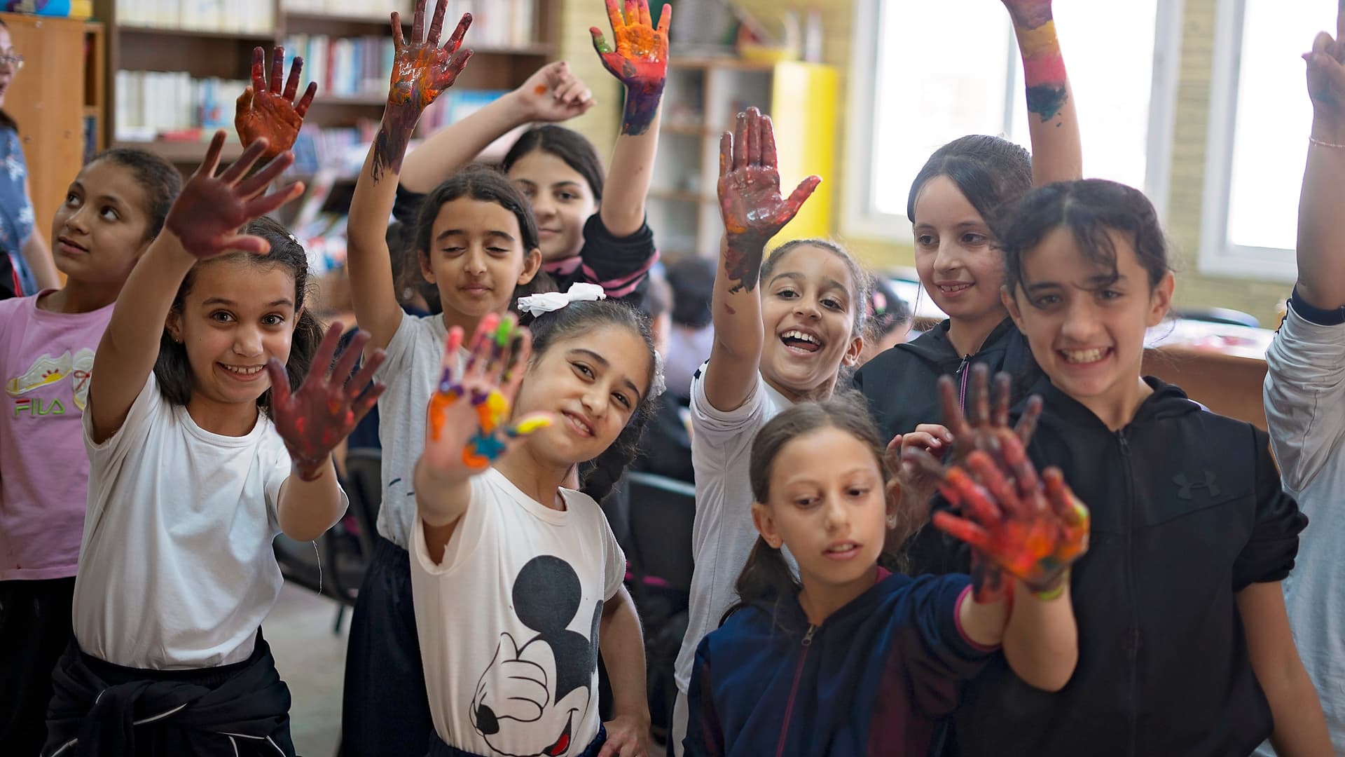 Foto: Ahmad Daghlas En grupp barn med målade händer i ett klassrum ler mot kameran.