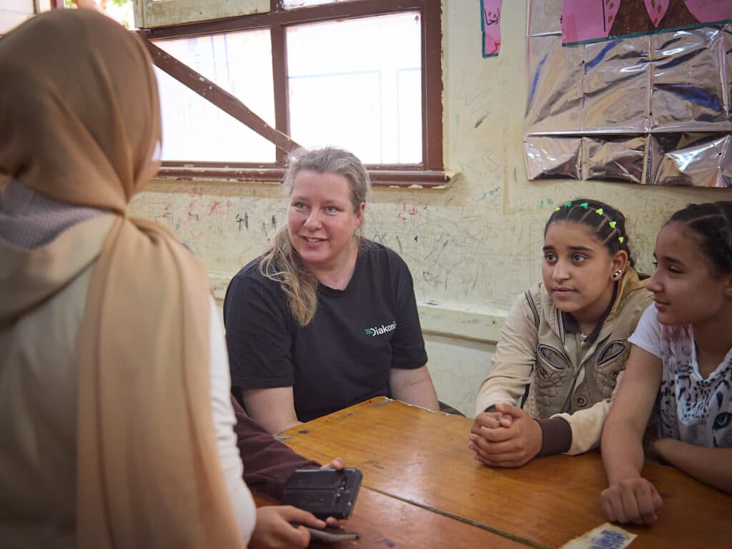 Foto: Sima Diab En kvinna med svart t-shirt sitter vid en skolbänk tillsammans med tre flickor.