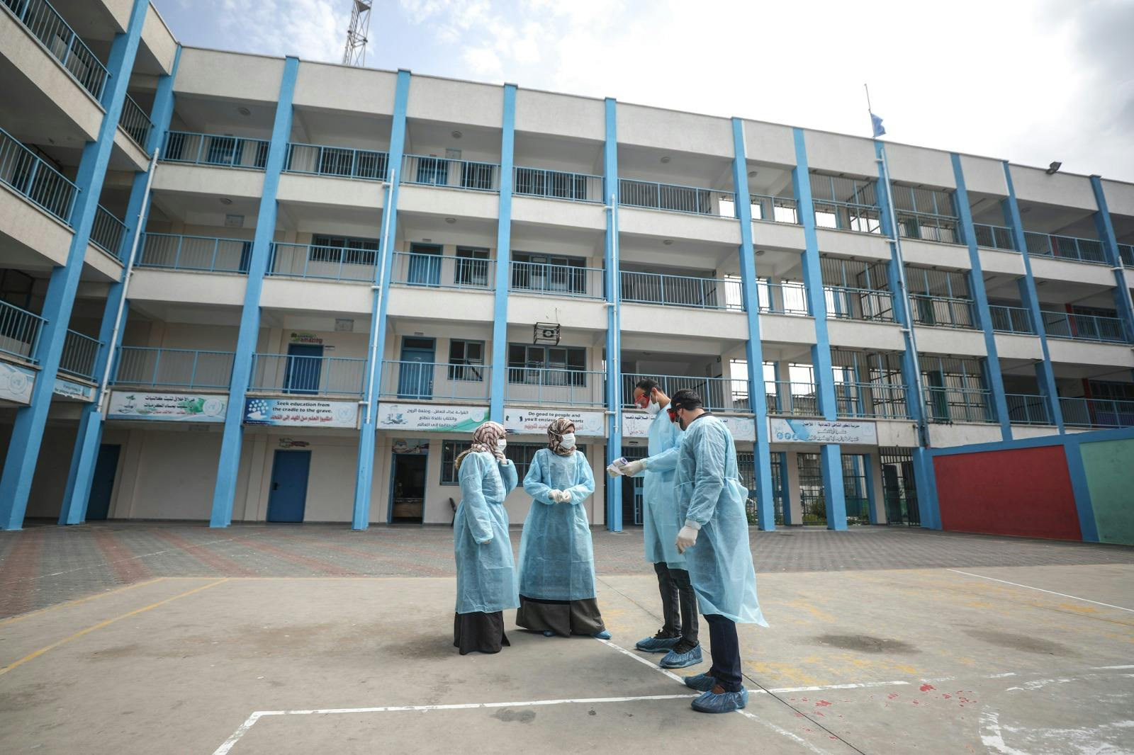 Health workers in protective gear discussing with each other, and in the background a tall building.