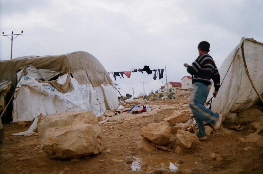 A boy walking through a camp with tents.