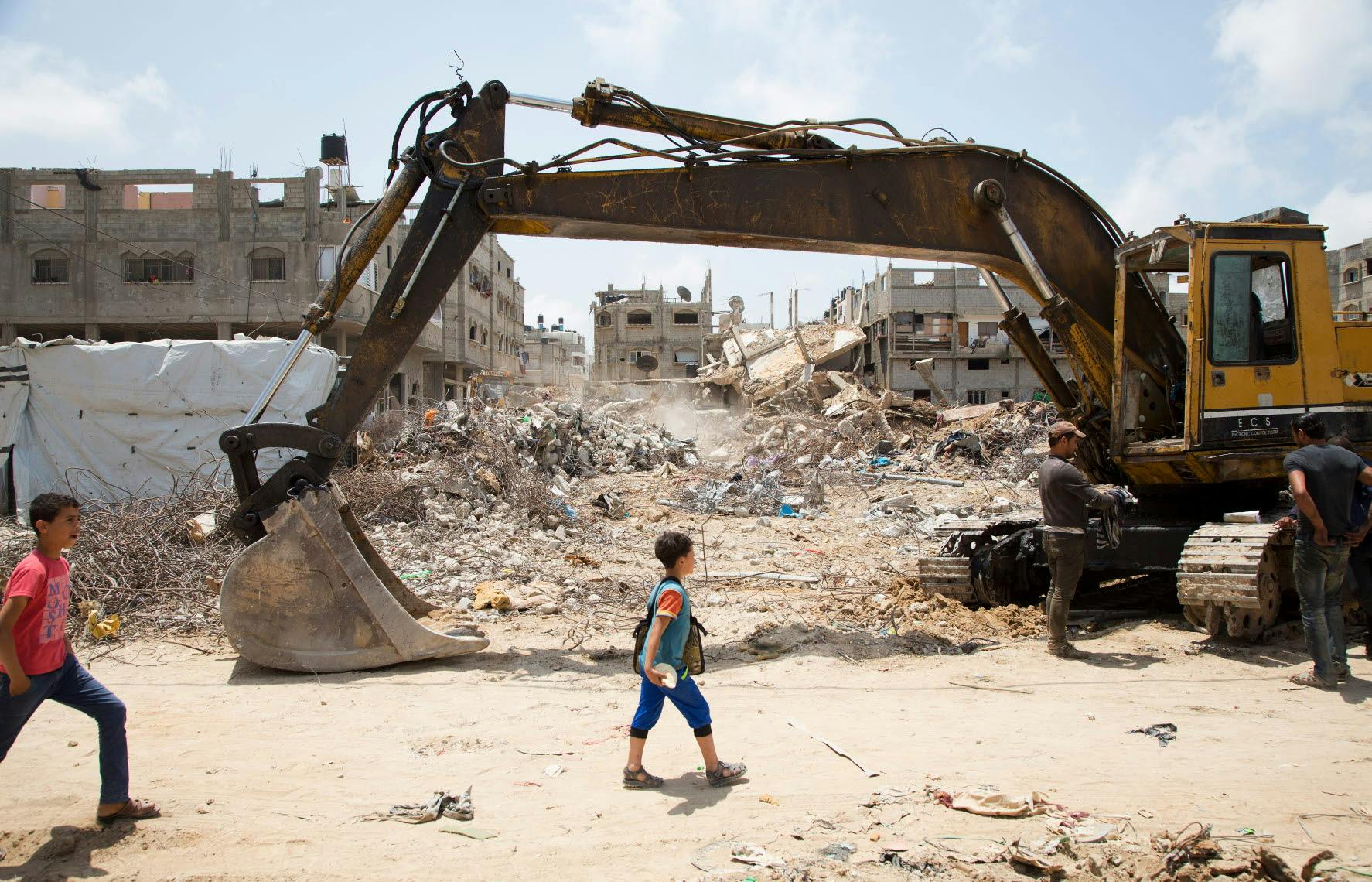 A child passes by a dredger with rubble in the background.