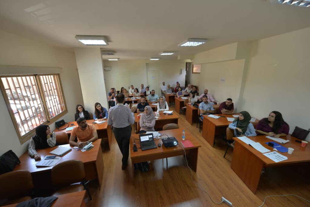 A classroom with many students listening to a teacher.