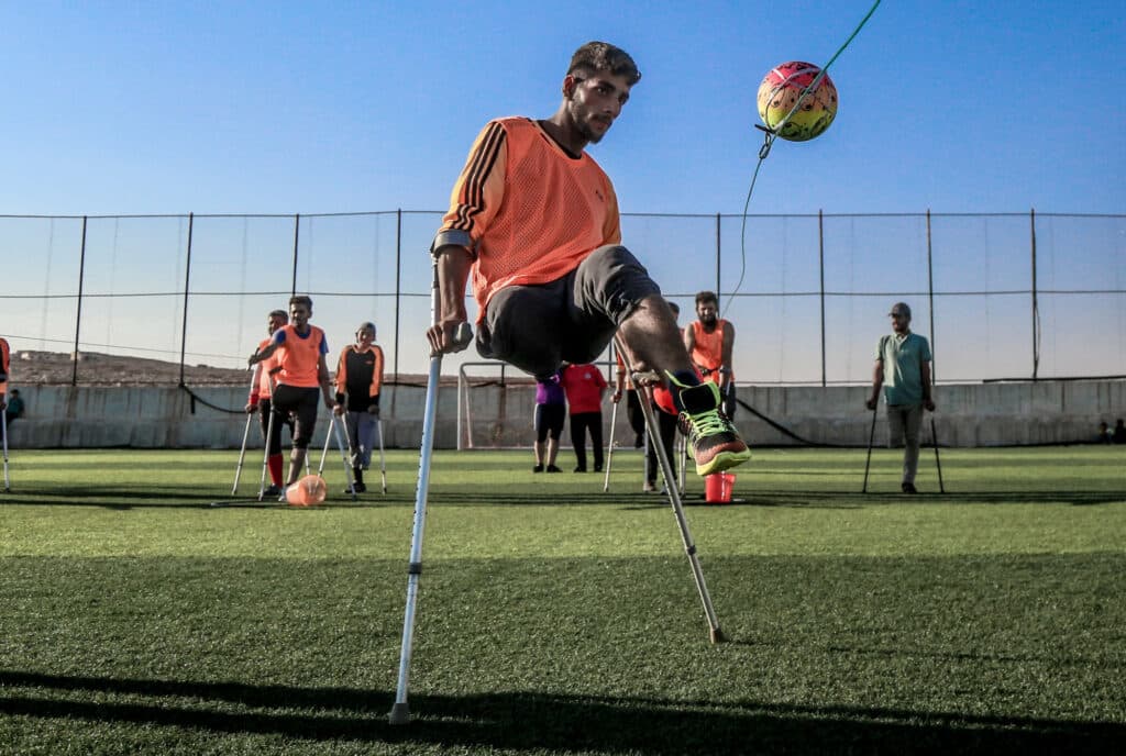 A football player with crutches hitting a ball.