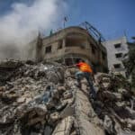 A man climbing on a pile of rubble that is still smoking after an air strike.